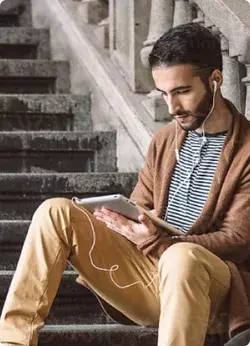 Student sitting on stairs with tablet device and earbuds